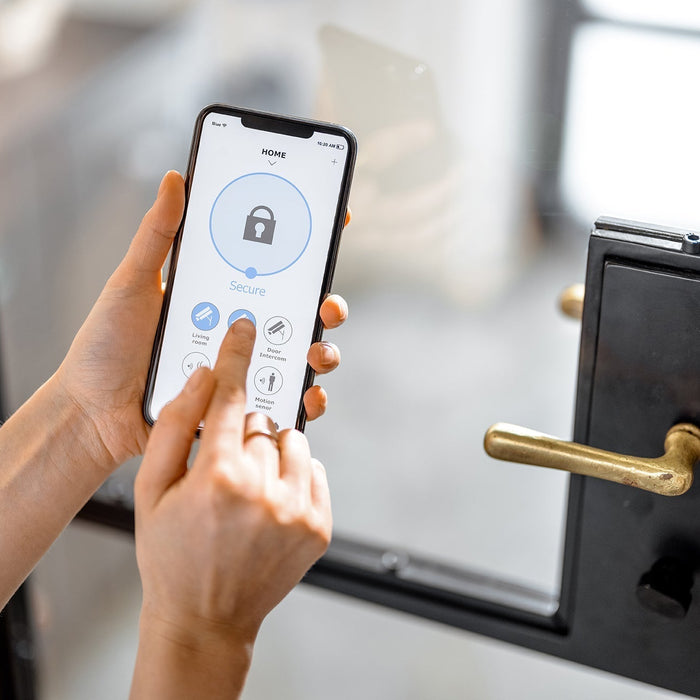 Person using a smartphone app to control a smart lock on a modern black-framed glass door with a brass handle.