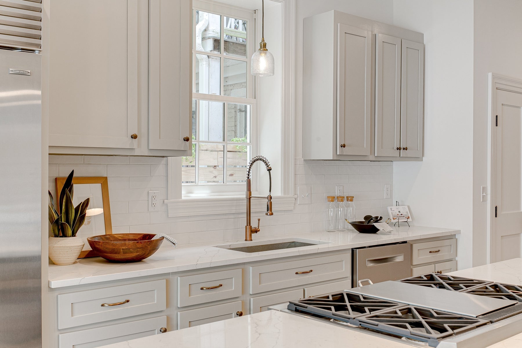 Bright kitchen with shaker-style cabinets, brass cabinet hardware, a spring pull-down faucet, and white quartz countertops.