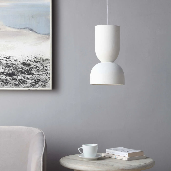 White pendant light hanging above a table with a cup and books against a gray wall with framed artwork.