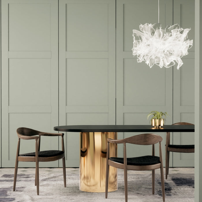 Modern dining area featuring a black and gold oval table, four sculpted wooden chairs, a white sculptural ceiling light, and sage green panelled walls.