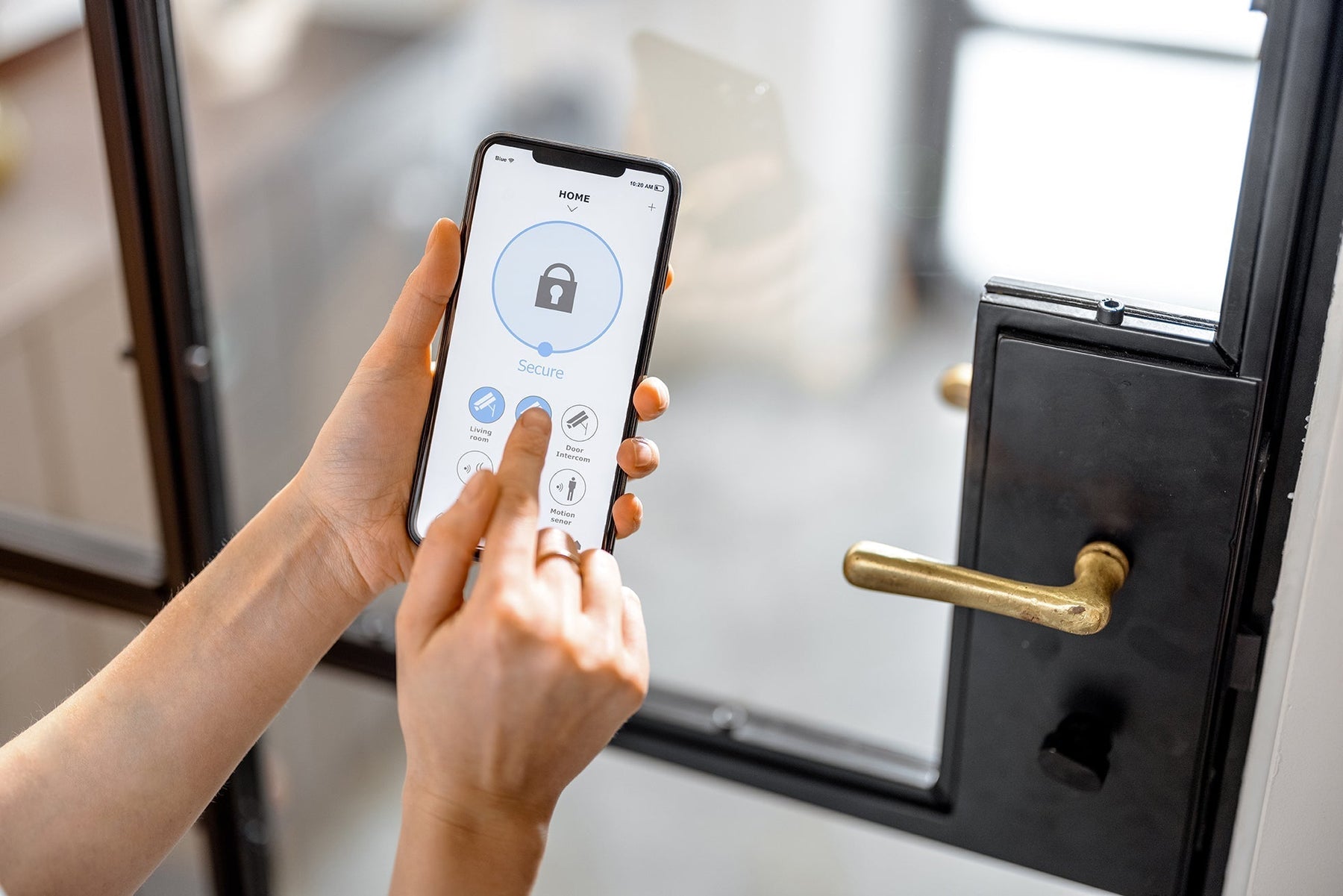 Person using a smartphone app to control a smart lock on a modern black-framed glass door with a brass handle.