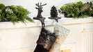 Two Christmas stockings hanging on a fireplace mantle decorated with greenery and a deer ornament.