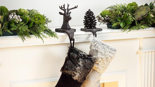 Two Christmas stockings hanging on a fireplace mantle decorated with greenery and a deer ornament.