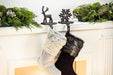 Two stockings hanging from a fireplace mantle decorated with greenery and festive decor.