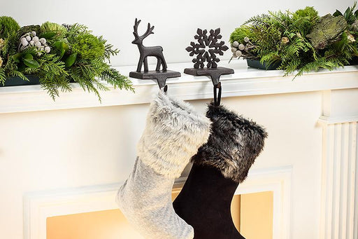 Two stockings hanging from a fireplace mantle decorated with greenery and festive decor.