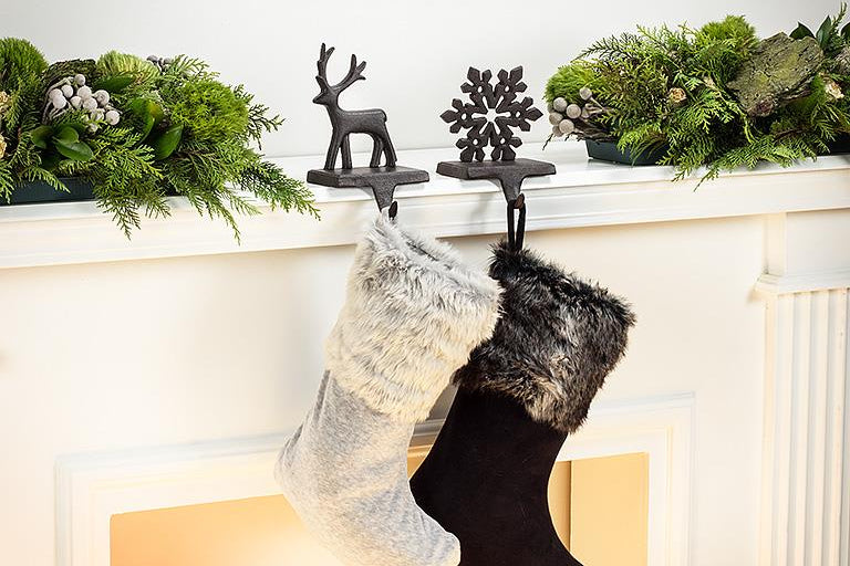 Two stockings hanging from a fireplace mantle decorated with greenery and festive decor.