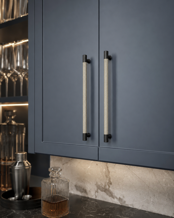 A close-up of dark slate blue kitchen cabinets with textured vertical bar handles, set against a marble backsplash and countertop with bar accessories.