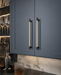 A close-up of dark slate blue kitchen cabinets with textured vertical bar handles, set against a marble backsplash and countertop with bar accessories.