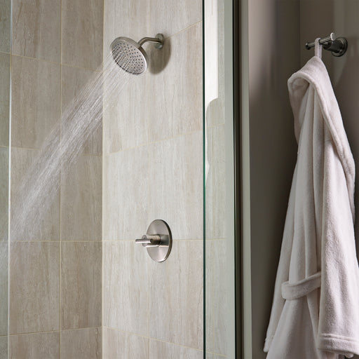 Pfister Contempra 1-handle shower set in brushed nickel, with water flowing from the round showerhead in a modern neutral toned shower.