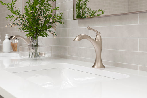 Pfister Rhen faucet in Brushed Nickel, installed on a white countertop with a modern sink and frameless mirror in a minimalist bathroom.