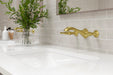 Pfister Rhen 2-handle wall-mount bathroom faucet in brushed gold, installed above a white undermounted sink on a sleek countertop in a contemporary bathroom.