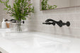 Pfister Rhen 2-handle wall-mount bathroom faucet in matte black, installed above a white undermounted sink on a white countertop in a modern bathroom.