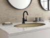 Pfister Tenet single-control bathroom faucet in matte black, installed on a white marble countertop with a matching gold sink, round mirrors, and minimalist decor.