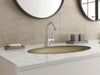 Pfister Tenet single-control bathroom faucet in polished chrome, installed on a white marble countertop with a matching gold sink, round mirrors, and minimalist decor.