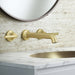 Pfister Tenet 2-handle wall-mount bathroom faucet in brushed gold, installed above a white undermounted sink on a simple, modern countertop.