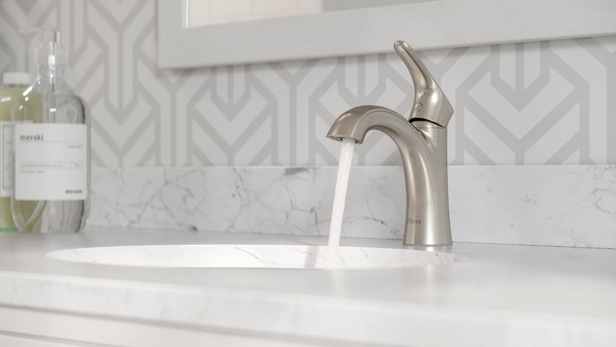Pfister Weller single-control bathroom faucet in brushed nickel, installed on a white countertop in a contemporary bathroom, with water flowing gracefully from the spout.