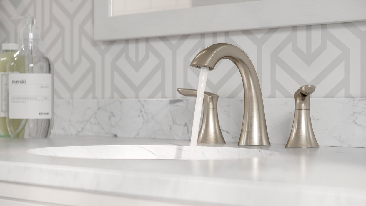 Pfister Weller 2-handle 8-inch widespread bathroom faucet in brushed nickel, installed on a white marble countertop in a contemporary bathroom, with water flowing gently from the spout.