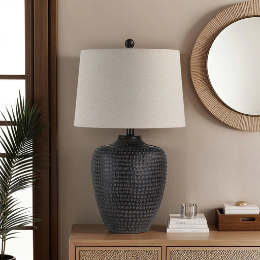 Decorative lamp with textured base on a wooden side table against a beige wall.