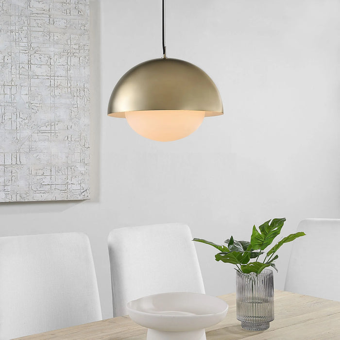 Gold pendant light fixture hanging above a dining table with chairs and a plant.