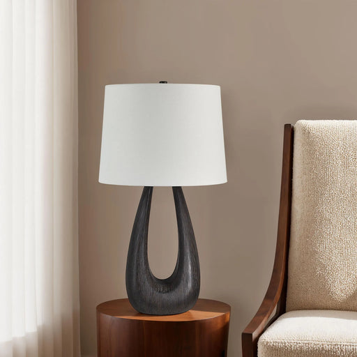 Table lamp with a white shade on a wooden side table next to a chair.