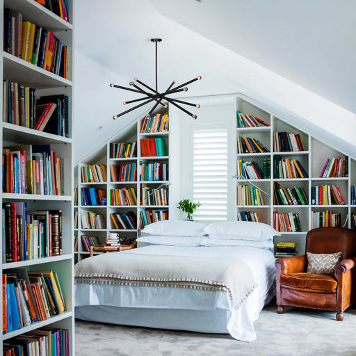 Bookshelf-lined bedroom with a bed and leather chair under a modern chandelier.