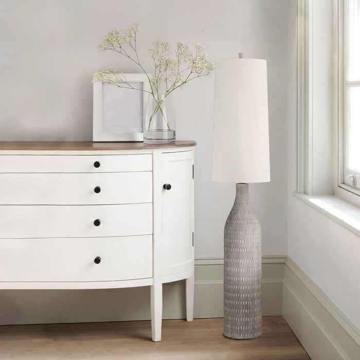 White dresser with a cream floor lamp and decorative items in a room.