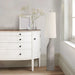 White dresser with a cream floor lamp and decorative items in a room.