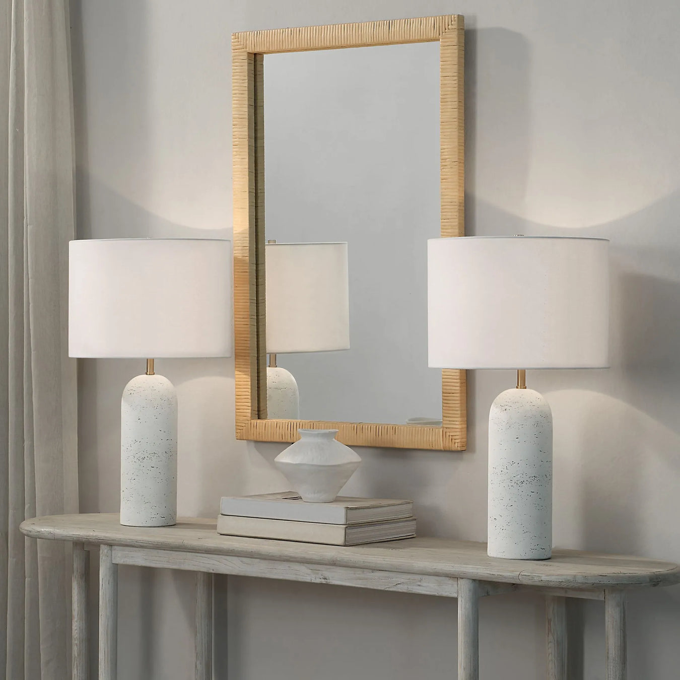 Two white table lamps on a wooden console table with a mirror above, against a gray wall.