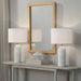 Two white table lamps on a wooden console table with a mirror above, against a gray wall.