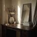 Wooden desk with lamp, vase, and mirror in a softly lit room