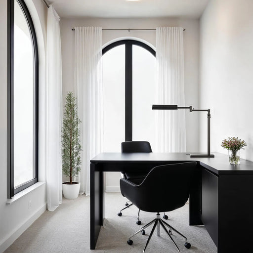 Modern home office with a black desk, chair, and lamp in a bright room.