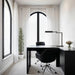 Modern home office with a black desk, chair, and lamp in a bright room.