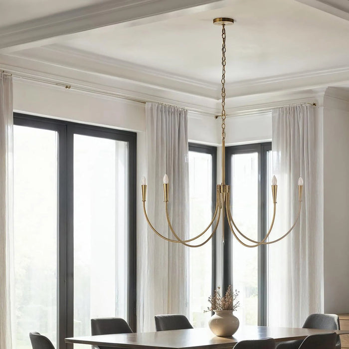 Gold chandelier hanging above a dining table with large windows and curtains in the background.