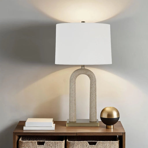 Table lamp with a concrete base and white shade on a wooden table against a gray wall.
