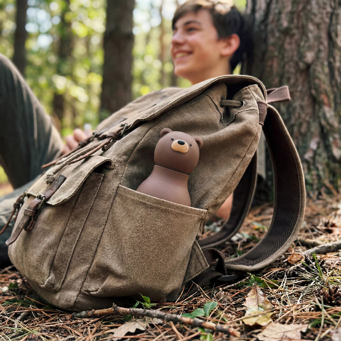 Asobu Besties Brown Bear insulated water bottle attached to a backpack outdoors