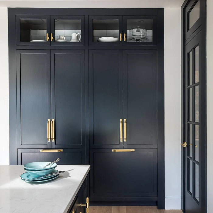 Buster + Punch Cross Pull Bar with Backplate in Brass finish on navy kitchen cabinetry and pantry doors