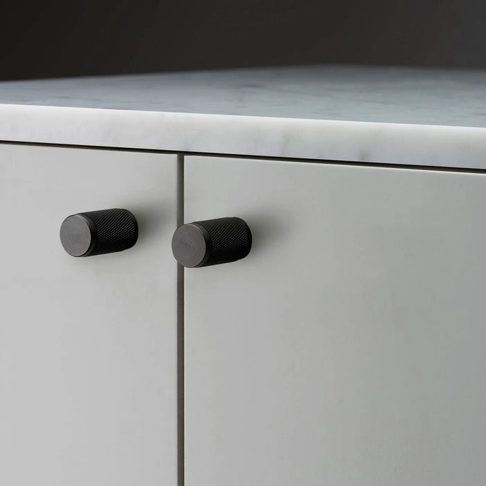 Close-up of Buster + Punch Furniture Knob Cross in smoked bronze finish on white cabinetry