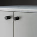 Close-up of Buster + Punch Furniture Knob Cross in smoked bronze finish on white cabinetry