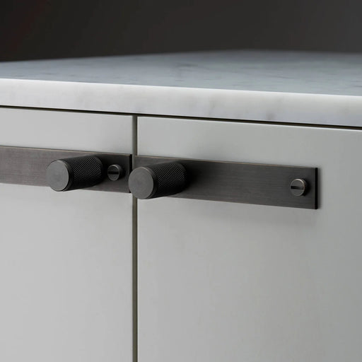 Close-up of Buster + Punch Cross Smoked Bronze furniture knob plate on cabinetry