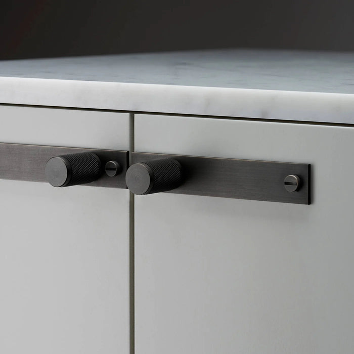 Close-up of Buster + Punch Cross Smoked Bronze furniture knob plate on cabinetry