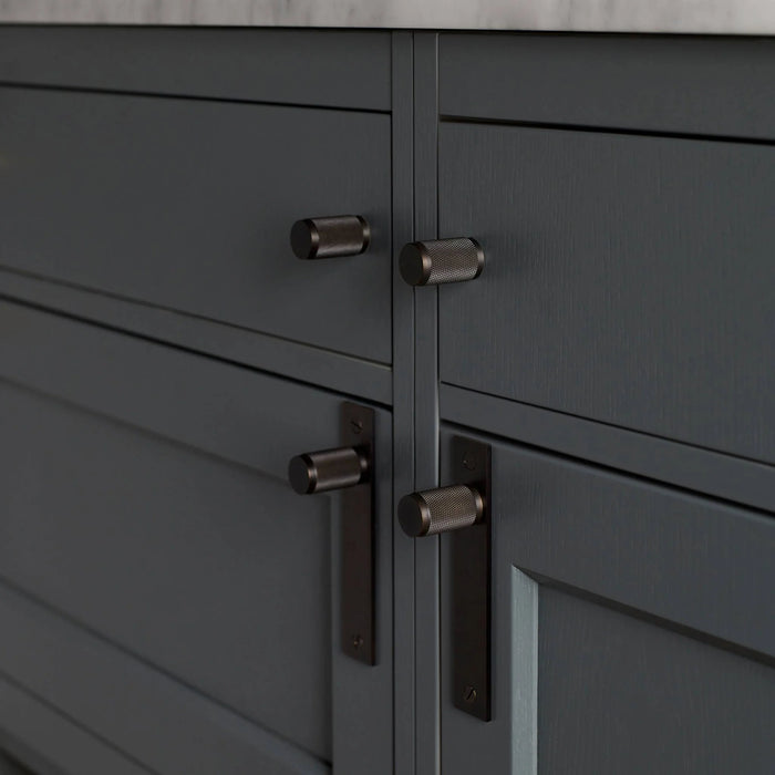 Smoked Bronze Buster + Punch furniture knob plate installed on dark cabinetry