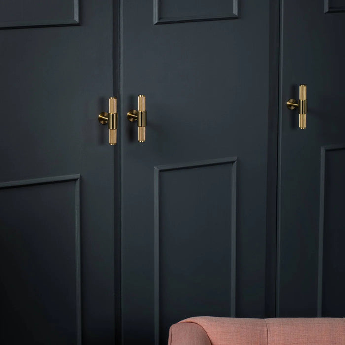 Brass Buster + Punch T-Bar Cross knobs installed on dark wardrobe doors