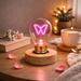 Butterfly neon LED light bulb on wooden base glowing on bedside table with cozy decor