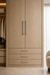 Häfele Elite Leather cabinet handles in matte gold finish with Oyster faux leather inserts installed on a modern oak wardrobe and matching drawer fronts.