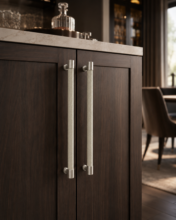 Two elite leather handles mounted on dark wood cabinet doors, shown in a real interior setting with a countertop and blurred room background.