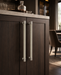 Two elite leather handles mounted on dark wood cabinet doors, shown in a real interior setting with a countertop and blurred room background.