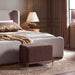 Renwil Meline brown linen ottoman stool styled at the foot of a bed