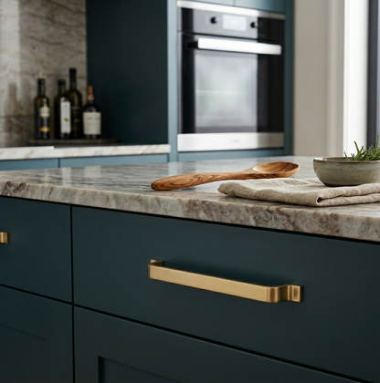 Richelieu 52003 modern metal cabinet pull in brushed aurum gold installed on a dark teal cabinet
