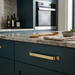 Richelieu 52003 modern metal cabinet pull in brushed aurum gold installed on a dark teal cabinet