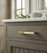 Richelieu 8655 modern metal pull in brushed aurum gold installed on a taupe cabinet drawer
